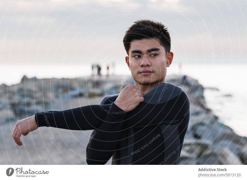 Ethnic sportsman stretching shoulders near sea workout fitness arm training exercise sporty sunset warm up asian ethnic male lifestyle athlete wellness young