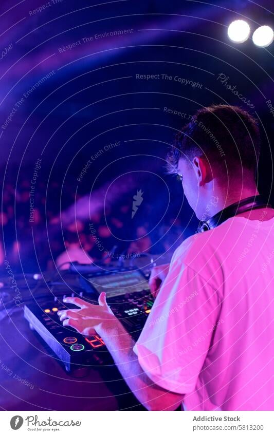 A DJ mixing on stage using board vertical rear view backview young caucasian dj music light occupation party purple millennial generation illuminated