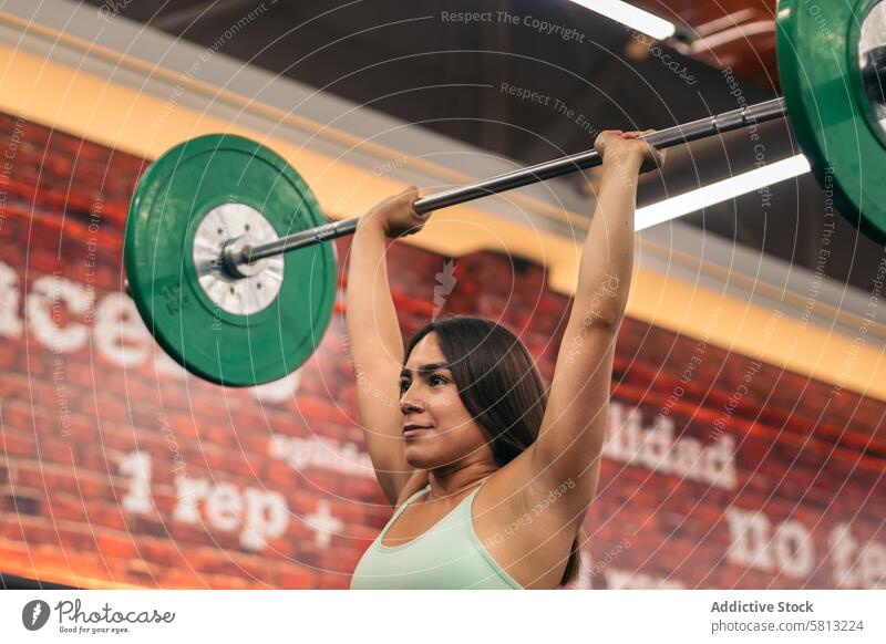 determined female athlete lifting barbell during weightlifting workout in gym while looking away muscular strength sport woman body people fit young fitness