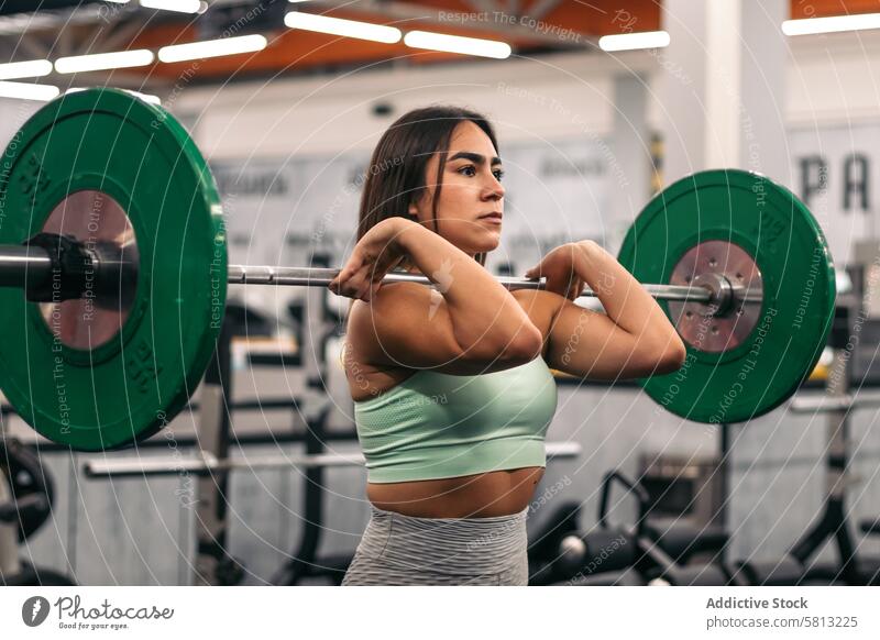 concentrated female athlete lifting barbell during weightlifting workout in gym while looking away muscular strength sport woman body people fit young fitness