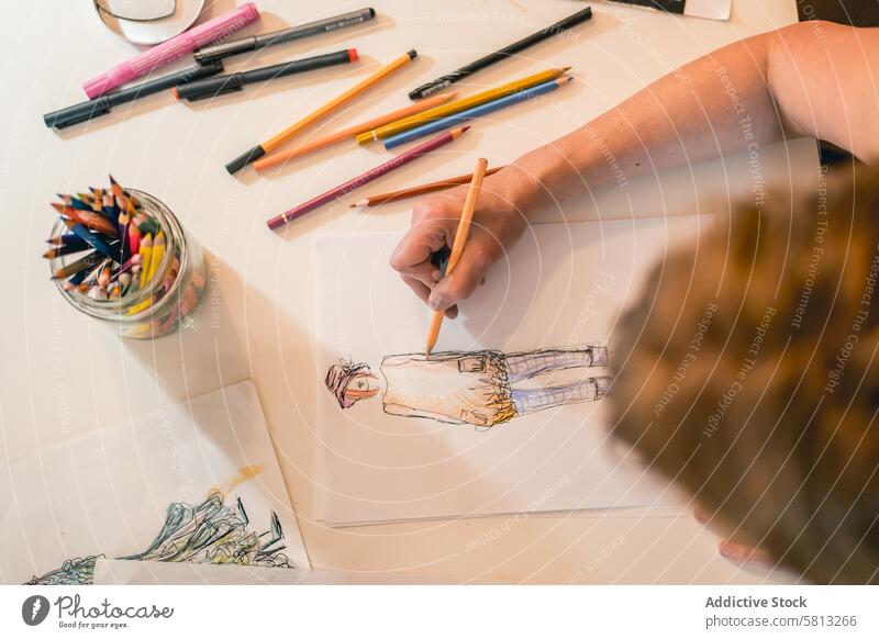 Top view of a fashion designer drawing a fashion sketch with colorful pencils 50s above clothing confidence confident creativity desk directly above dressmaker