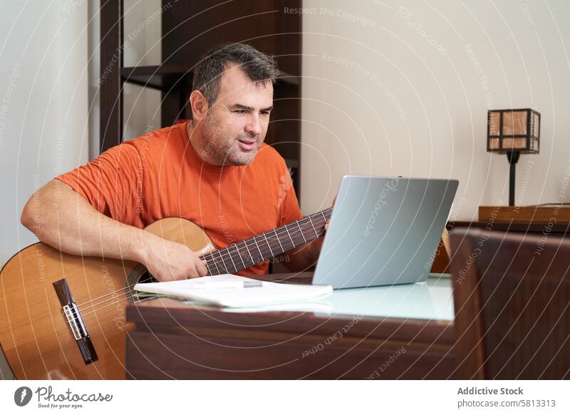 a man with laptop in online guitar lessons learning harmonics musician musical sitting adult computer playing internet male home guitarist instrument song