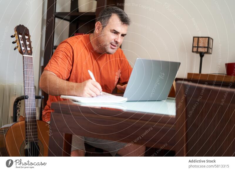 a man with a laptop computer in online guitar lessons writes scales and chords classical learning tune guitarist musician musical sitting adult playing internet