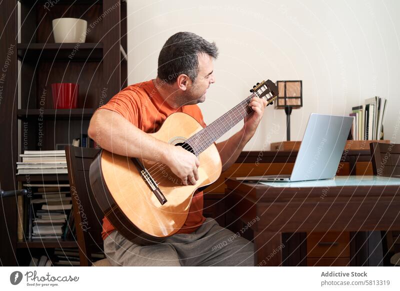 a man with laptop computer in online guitar lessons learning chords classical guitarist musician musical sitting adult playing internet male home instrument