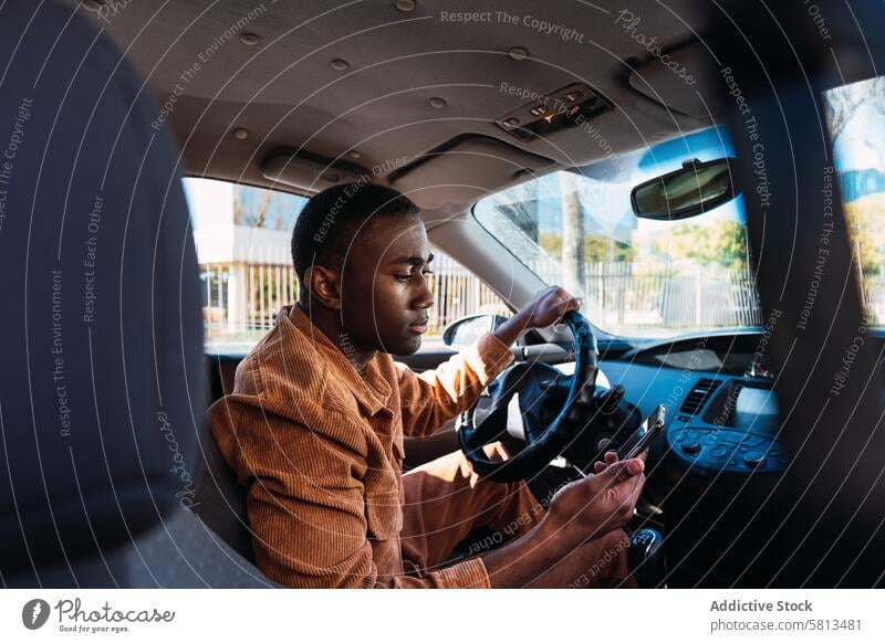 Black driver browsing smartphone in car man automobile internet online commute modern steering wheel black african american surfing transport trendy style