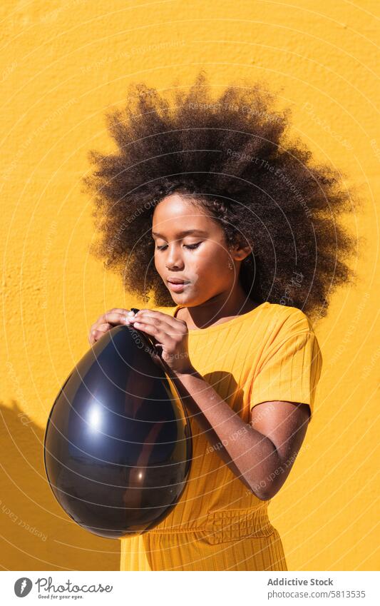Black girl blowing party balloon black yellow afro curly hair colorful vivid inflate child kid teenage hairstyle ethnic african american bright lifestyle female