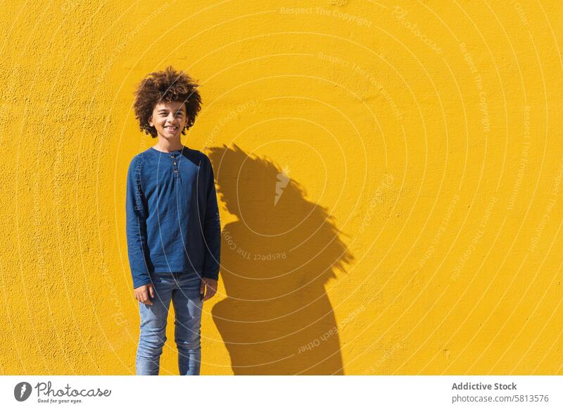 Ethnic boy with curly hair standing on yellow wall afro colorful bright kid teen gesture positive male child african american black ethnic teenage vibrant