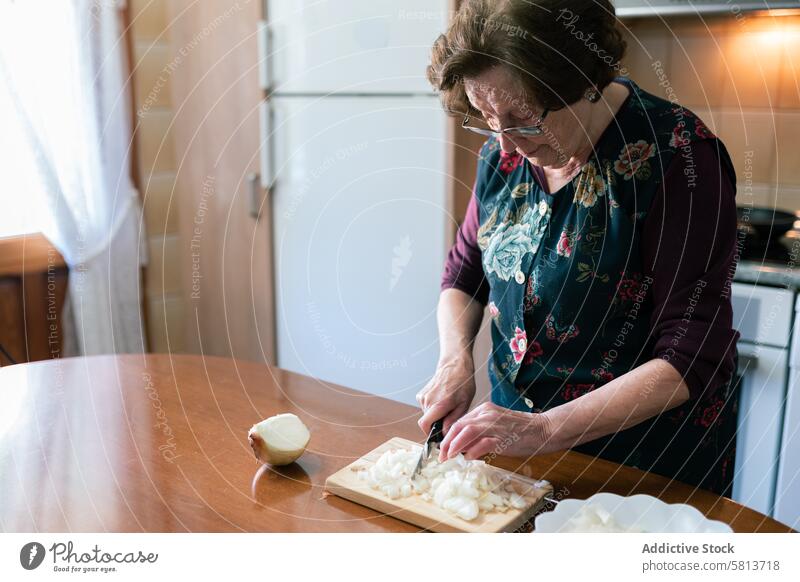 Old woman chopping onion to prepare croquettes at home old cooking preparation kitchen knife senior food board cutting board concentration sharp stand homemade