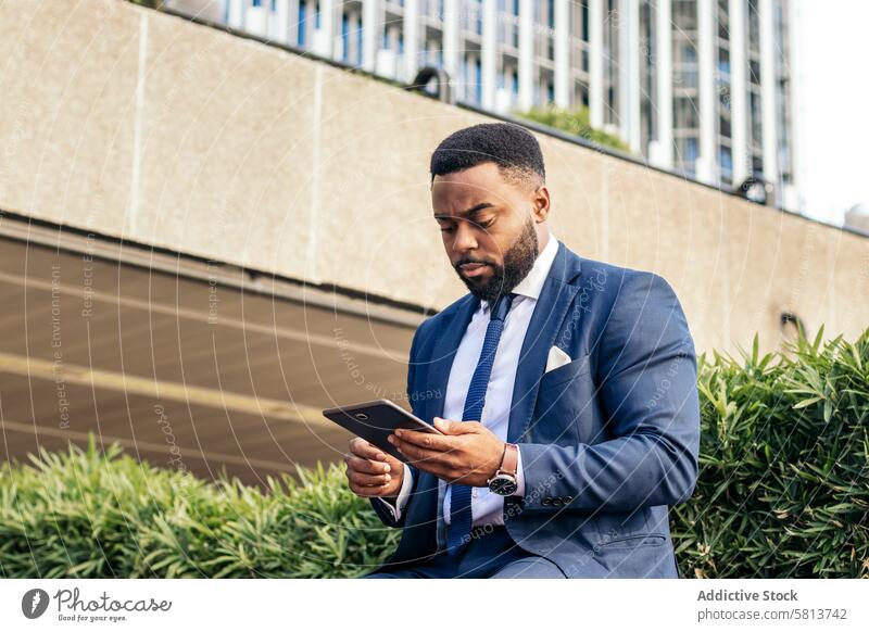 Low angle of a black businessman in a suit using a tablet outside. He looks concentrated meeting team professional executive success entrepreneur finance
