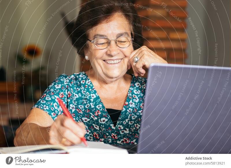 Old woman with glasses using a laptop and a notebook at home senior technology computer mature happy female internet person people sitting lifestyle adult