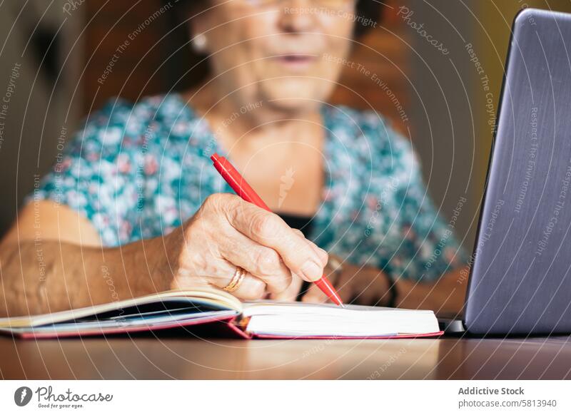 Old woman using a laptop and a notebook at home senior technology computer glasses mature happy female internet person people sitting lifestyle adult smiling