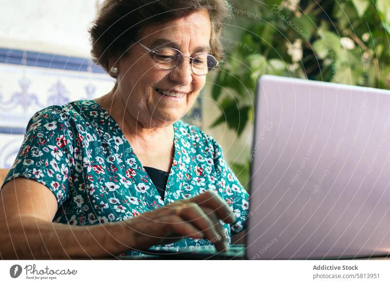 Senior woman with glasses using a laptop and a notebook at home senior technology computer mature happy female internet person people sitting lifestyle adult