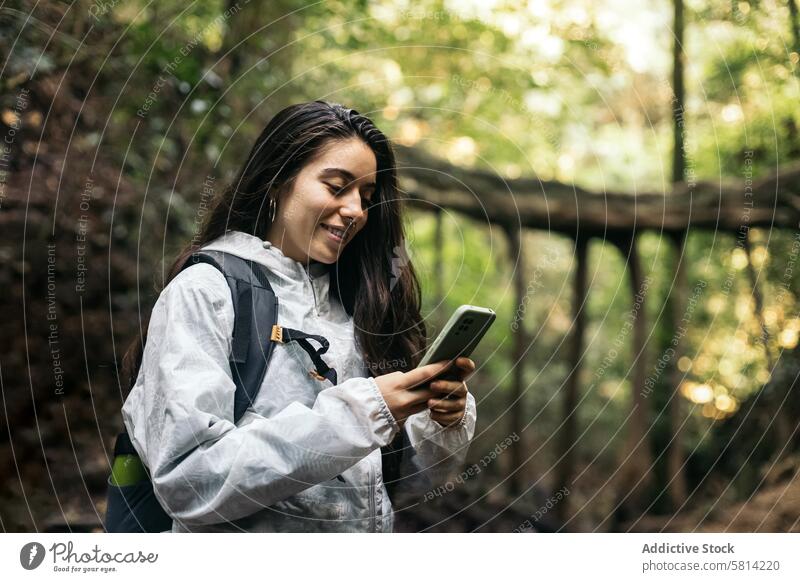 Cheerful woman using smartphone in the jungle forest portrait outdoors nature lifestyle people vacation leisure looking hiking tree travel backpack autumn