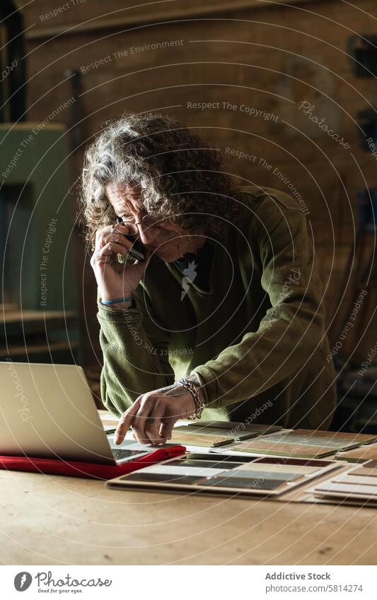 Man talking on smartphone and typing on laptop in workshop man carpenter using order phone call sample male joinery industry craft artisan craftsman manufacture
