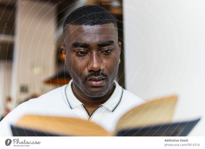 Serious African American male reading book in cafeteria man alone serious hobby novel thoughtful african american black adult pensive story concentrate