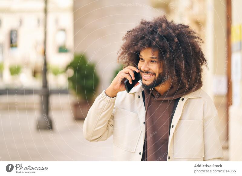 portrait of a smiling young man with long curly hair talking on the phone afro happy person adult mobile technology handsome businessman guy street smart