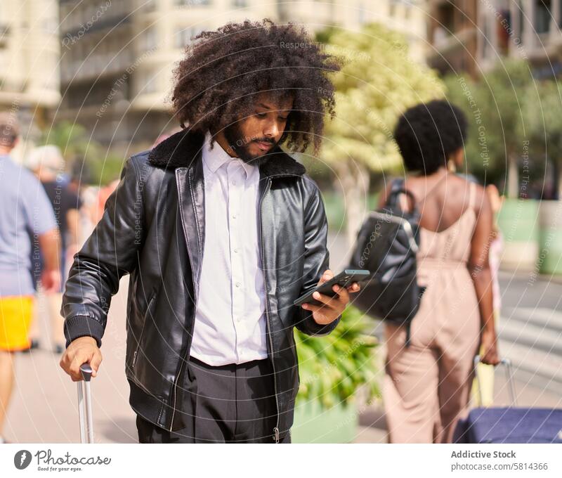a young man with afro hair in the city with a suitcase using a cell phone walking around mobile travelling person trip baggage luggage vacation journey tourism