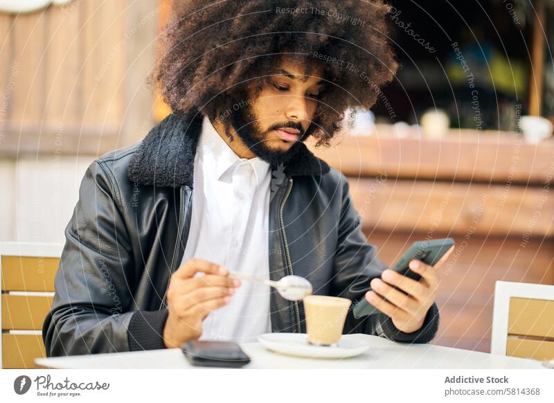 an african-american man looking at his cell phone while drinking coffee portrait afro hair having hot terrace male young adult person handsome lifestyle guy