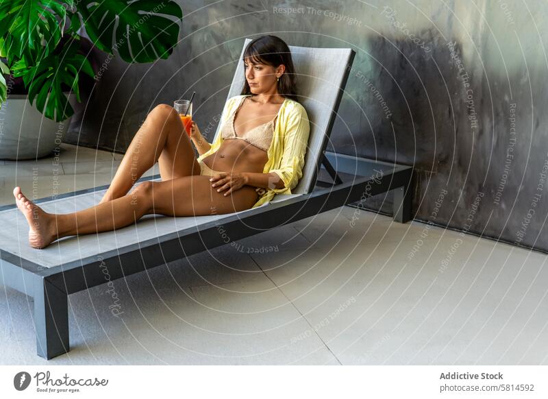 A beautiful woman is resting on a lounge chair in the pool area of a fancy hotel. Copy space adult attractive beauty beverage bikini carefree caucasian charming