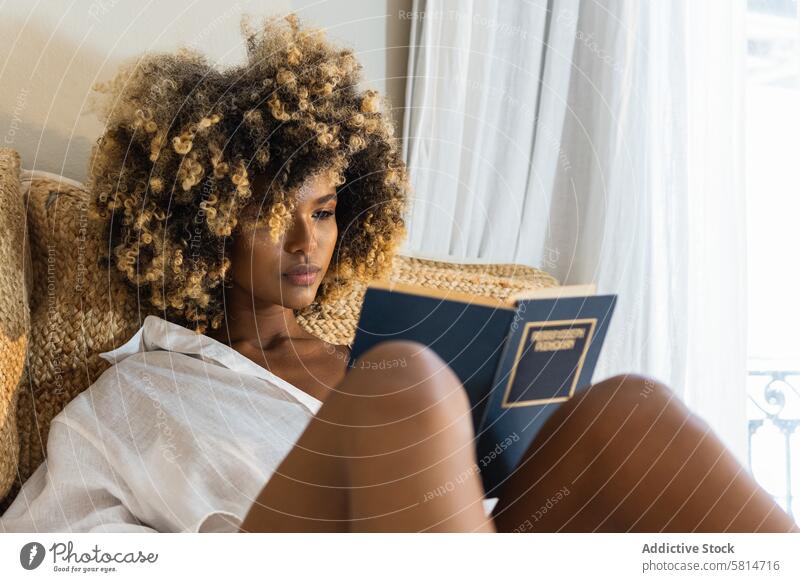 Young black woman sitting on bed and reading book hobby bedroom morning weekend leisure literature female home novel attractive at home pillow free time fiction