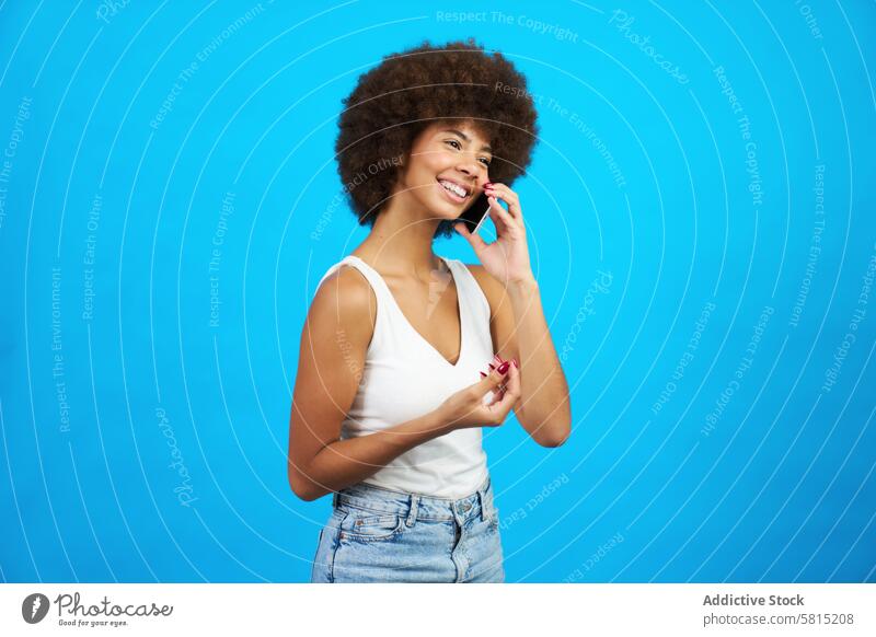 young latina woman with afro hair smiling talking on a mobile phone blue background nodding female person happy beauty black american portrait attractive adult