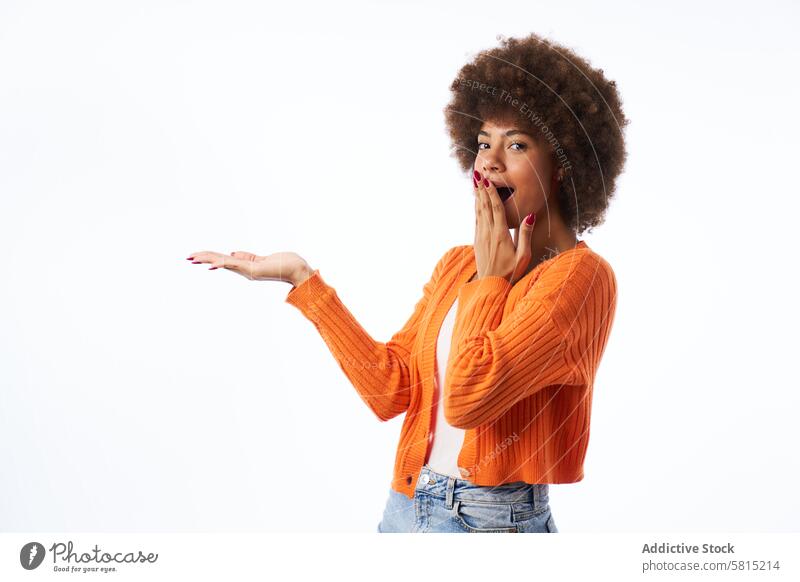 young latina woman with afro hair with surprised gesture points with hand isolated white background portrait studio jacket orange color person female happy