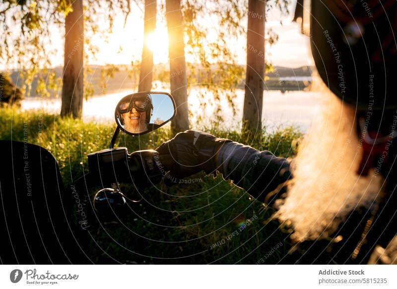 Senior Biker's Reflection in Motorcycle Mirror at Sunset reflection motorcycle mirror senior man smiling helmet sunglasses beard smile happy sunset trees lake
