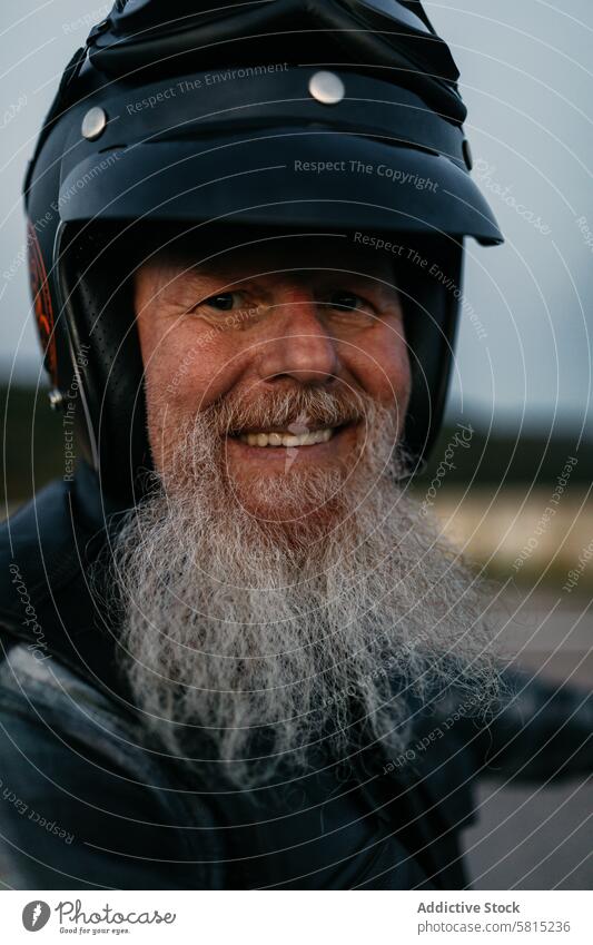 Smiling senior biker with helmet and leather jacket man smiling motorcycle looking at camera elderly rider portrait cheerful beard white beard smile happy