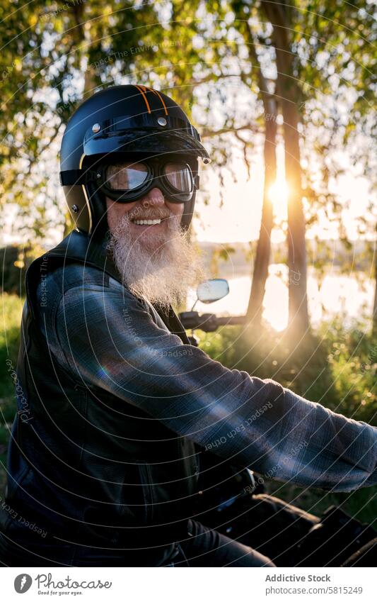 Senior biker enjoying sunset ride on motorcycle senior elderly male beard smile happy helmet goggles leather jacket outdoor looking at camera leisure activity