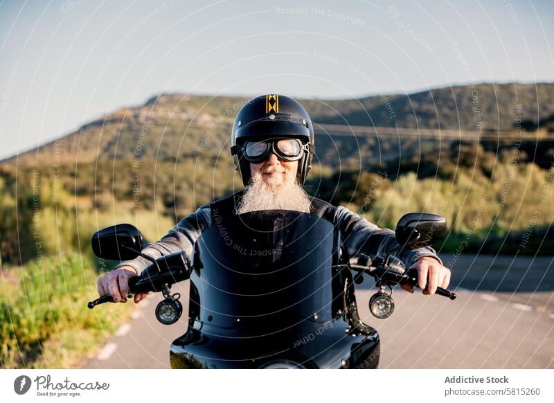 Senior biker with beard enjoying a ride senior man motorcycle helmet outdoors looking at camera vehicle transportation leisure lifestyle adventure travel road