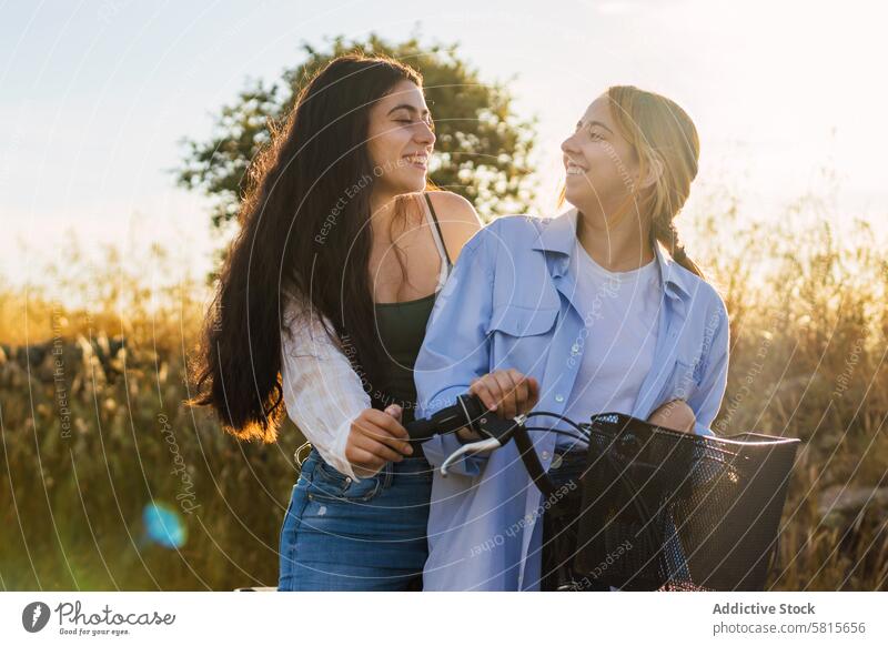 two young women on a bike in a field during sunset lifestyle bicycle woman summer nature happy sky girl leisure people couple together happiness spring outdoor