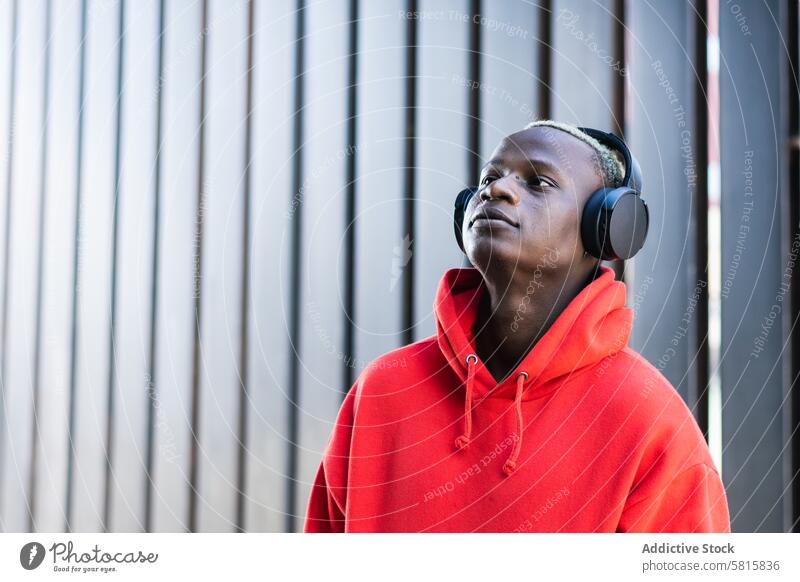 Content black young man listening to music in headphones enjoy meloman trendy happy relax song male african american ethnic style hoodie wireless sound glad