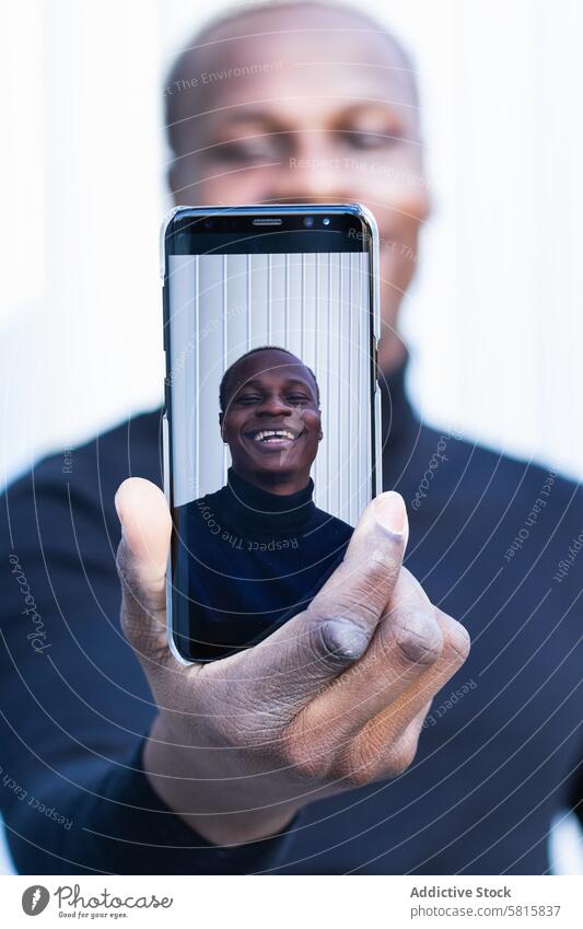 Joyful African American male taking selfie on smartphone in sunlight man smile cheerful joy screen street enjoy self portrait happy mobile young