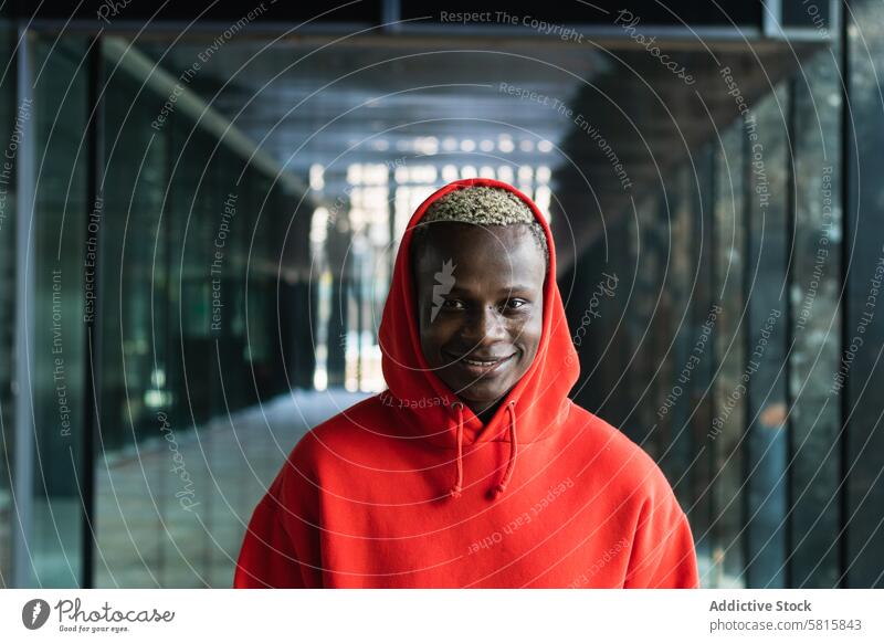 Smiling young black guy looking at camera in contemporary building man adjust hood smile self assured passage style cool portrait individuality personality male