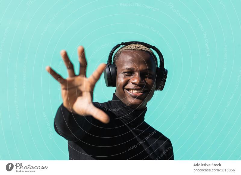 Stylish young black guy listening to music in headphones and reaching out hand man gesture smile enjoy positive portrait street happy cheerful male