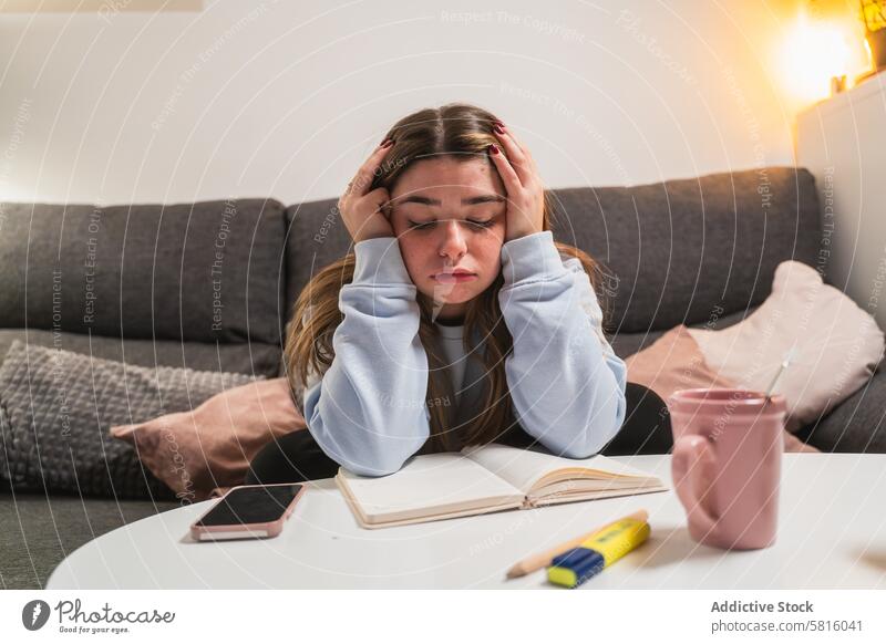 Stressed young girl studying at home stressed tired book smartphone cup woman education learning student anxiety overwhelmed sitting couch indoor frustration