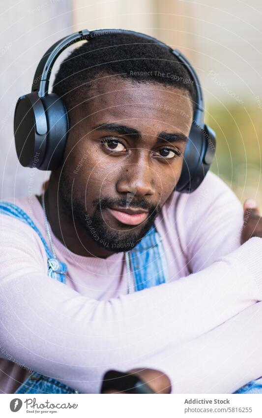 Stylish black man listening to music in headphones hipster cool urban independent song style male ethnic african american outfit street modern gadget wireless