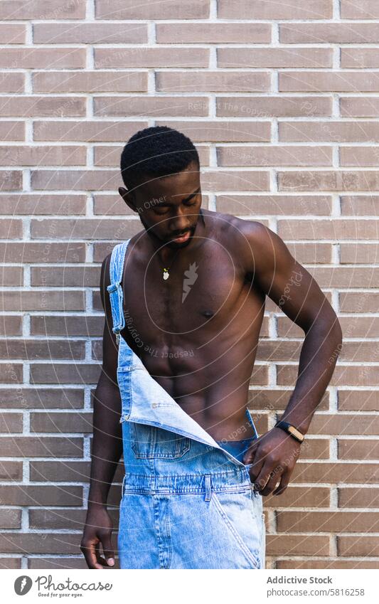 Fit black man in overalls in city naked torso fit model handsome shirtless muscular outfit male ethnic african american apparel denim brick wall stand urban