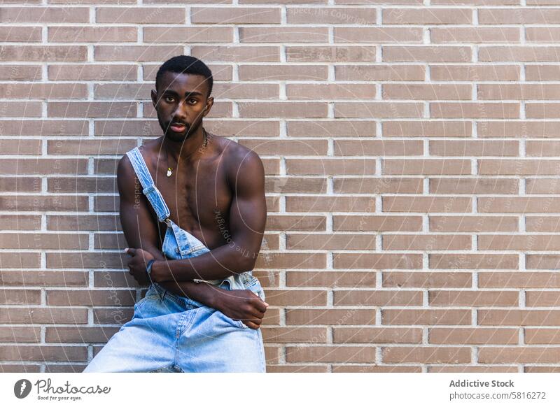Fit black man in overalls in city naked torso fit model handsome shirtless muscular outfit male ethnic african american apparel denim brick wall stand urban