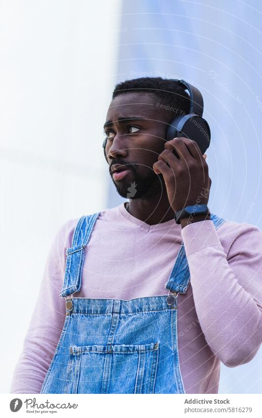 Stylish black man listening to music in headphones hipster cool urban independent song style male ethnic african american outfit street modern gadget wireless