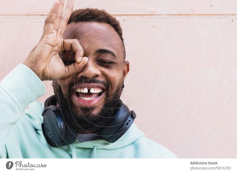 Delighted ethnic hipster man with okay gesture cheerful finger happy headphones beard casual adult african american black having fun playful sign male smile
