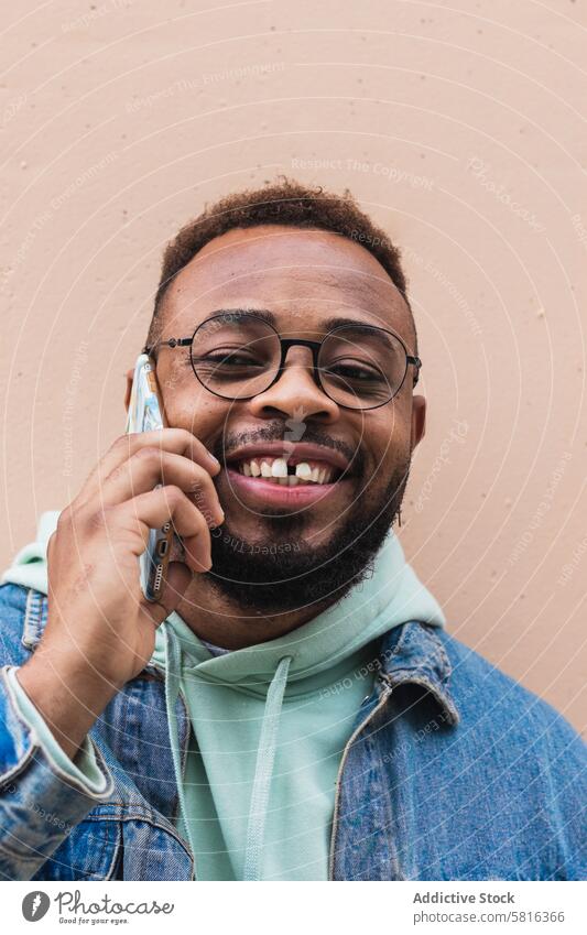 Cheerful black man talking on phone near wall smartphone cheerful laugh hipster casual conversation communicate adult african american ethnic beard male