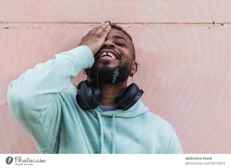 Delighted ethnic hipster man covering eye cheerful gesture happy headphones beard casual adult african american black having fun playful sign male smile