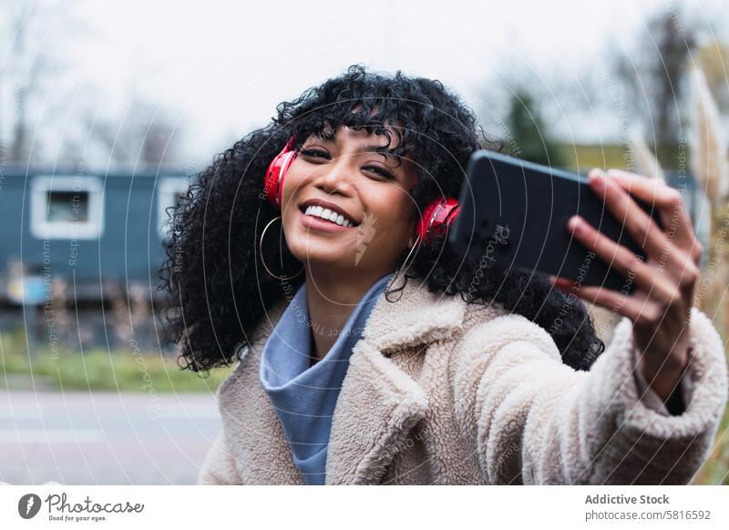 Black woman taking selfie on street smartphone headphones using music listen chill female african american woman black woman city portrait smile positive autumn