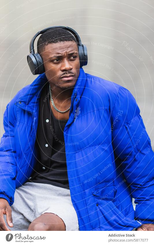 Black man listening to music in city calm song headphones wireless melancholy street male ethnic black african american stone outfit hipster border warm jacket