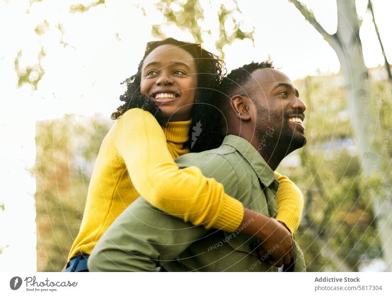 smiling black man giving piggyback ride to happy black girl. Side view fun people together carrying woman male family love portrait young african boy cheerful