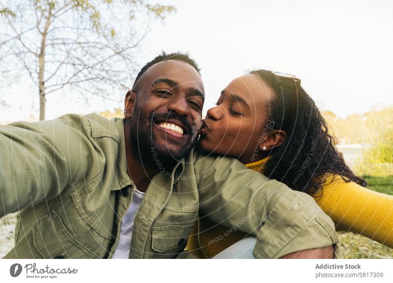 afro american couple taking a selfie kissing on the cheek. sitting in a park woman happy young african black people cheerful portrait female smiling boyfriend