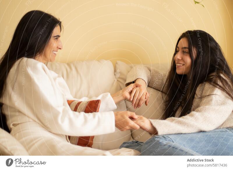 Mother and daughter smiling and holding hands adult love sofa mother home talking lifestyle family female people girl mature parent together sitting senior