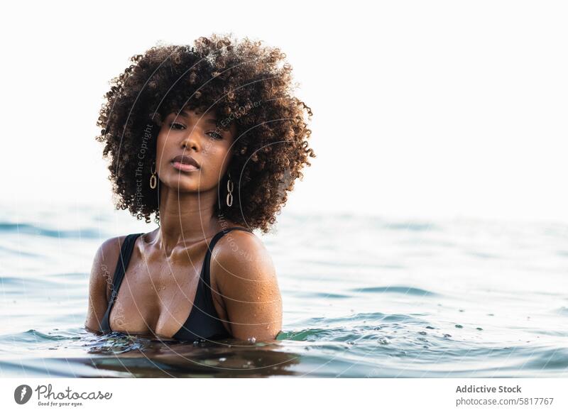 Black woman in bikini in sea water afro hairstyle appearance charming calm summer female ethnic black african american swimwear holiday tranquil peaceful stand