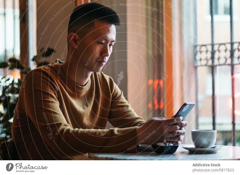 Asian man sitting in coffee shop using smartphone. restaurant young lifestyle happy asian people cafe technology drink mobile internet adult looking smiling